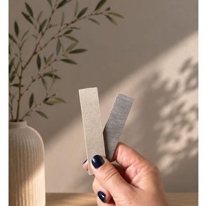 May include: Two rectangular material swatches, one in a light beige and one in a dark gray, are held up. The text at the top reads "Unsere Naturt&ouml;ne" followed by "PLA MIT HOLZANTEIL HELL - PLA MIT HOLZANTEIL DUNKEL" indicating light and dark wood-infused PLA.