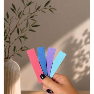 May include: Four rectangular strips in neon pink, blue, purple, and light blue. The text at the top reads "Unsere Knalligen II" followed by "NEONPINK - BLAU - LILA - HELLBLAU". The strips have a textured finish and are held in a fan shape.