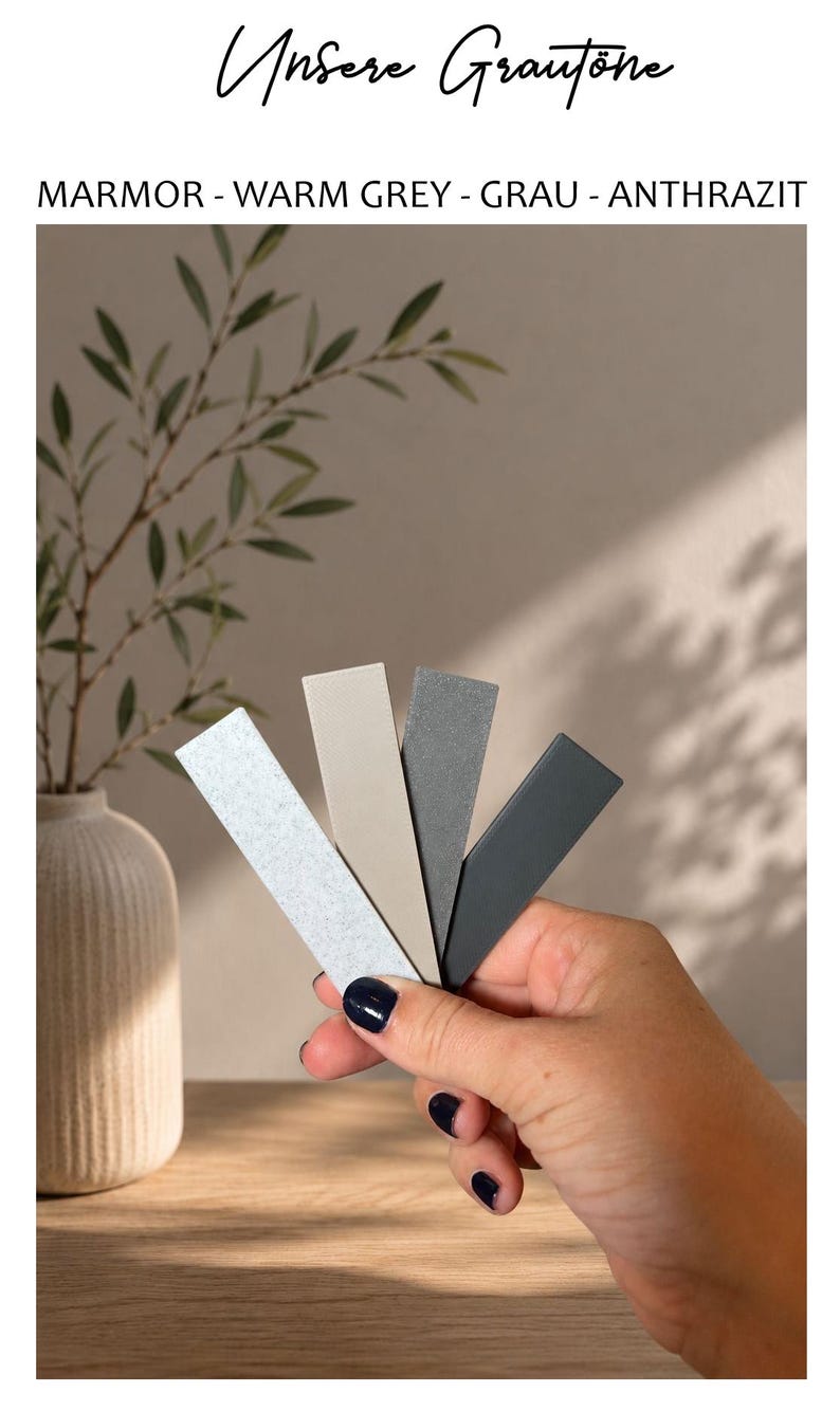 May include: Four rectangular color swatches in shades of light grey marble, warm beige, medium grey, and dark charcoal. The text at the top reads "Unsere Graut&ouml;ne" followed by "MARMOR - WARM GREY - GRAU - ANTHRAZIT" in black lettering.