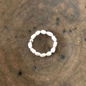 May include: A white pearl ring with a silver accent. The ring is made of small, oval-shaped pearls.