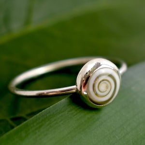 Könnte beinhalten: Ein silberner Ring mit einer weißen Muscheleinlage mit einem Spiralmuster.
