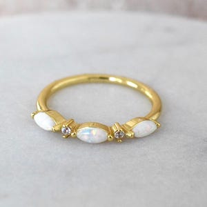 Könnte beinhalten: Ein goldener Ring mit drei weißen Opalen in Marquise-Form und zwei kleinen runden, klaren Diamanten.
