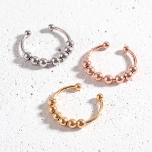 Könnte beinhalten: Drei offene Ringe, die jeweils mit einer Reihe kleiner, beweglicher Metallperlen entlang der Ringschiene versehen sind. Ein Ring ist silberfarben, einer roségoldfarben und einer goldfarben. Die Ringe sind in Dreiecksform angeordnet.