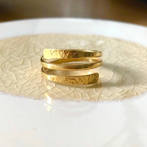 Könnte beinhalten: Ein goldfarbener, gehämmerter Metallring mit einem Spiraldesign. Der Ring besteht aus drei Bändern, die miteinander verdreht sind.