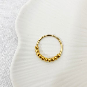 Könnte beinhalten: Ein goldener Perlenring mit schlichtem Design. Der Ring besteht aus einem dünnen Metallband mit einer Reihe kleiner, runder Perlen.