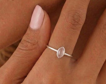 Può includere: Un delicato anello d'argento con una gemma ovale rosa chiaro. L'anello ha una fascia sottile e la gemma è incastonata in uno stile minimalista. L'anello è un gioiello.