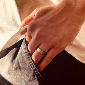 Könnte beinhalten: Eine Hand mit einem silbernen Bandring. Der Ring ist schlicht und hat ein flaches, breites Band.