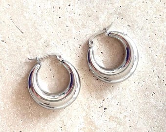 Può includere: Un paio di orecchini a cerchio d'argento con un design spesso e arrotondato.