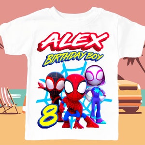May include: White t-shirt with a Spiderman theme. The shirt features three Spiderman characters, a red and blue Spiderman, a black and red Spiderman, and a white and blue Spiderman. The shirt also has the text "ALEX BIRTHDAY BOY" and the number "8" in yellow.