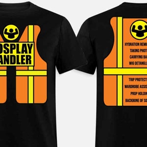 May include: Black t-shirt with a bright orange and yellow safety vest design. The front of the shirt says "COSPLAY HANDLER". The back of the shirt lists responsibilities of a cosplay handler, including "hydration reminders", "taking photos", "carrying bags", "wig detangling", "trip protection", "wardrobe assistance", "prop holding", and "backbone of society".
