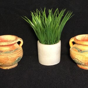 May include: Two small terracotta pots with green and yellow painted designs, each with two handles, and a small white planter with green grass.