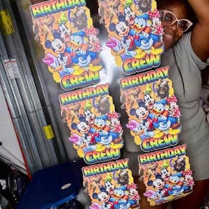 Könnte beinhalten: Mehrere farbenfrohe Geburtstagsdekorationen mit Micky Maus, Donald Duck und anderen Zeichentrickfiguren. Die Dekorationen tragen die Worte "Birthday Crew" in einer Regenbogen-Schriftart. Das Bild zeigt eine Person, die die Dekorationen hält.