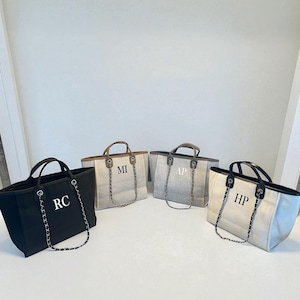 May include: Four tote bags in various colours, each with initial letters. The bags feature black, beige, and grey fabric with black handles and silver chain straps. Each bag displays different initials: RC, MI, AP, and HP.