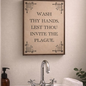以下が含まれることがあります： 「WASH THY HANDS, LEST THOU INVITE THE PLAGUE.」と書かれた額入りの看板が、クロム製の蛇口が付いた洗面台の上に掛けられています。茶色のソープディスペンサーと白いタオルの山も確認できます。