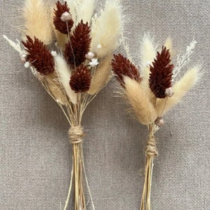 May include: Two bouquets of dried pampas grass and brown dried flowers tied with twine. The bouquets are arranged on a beige textured surface.