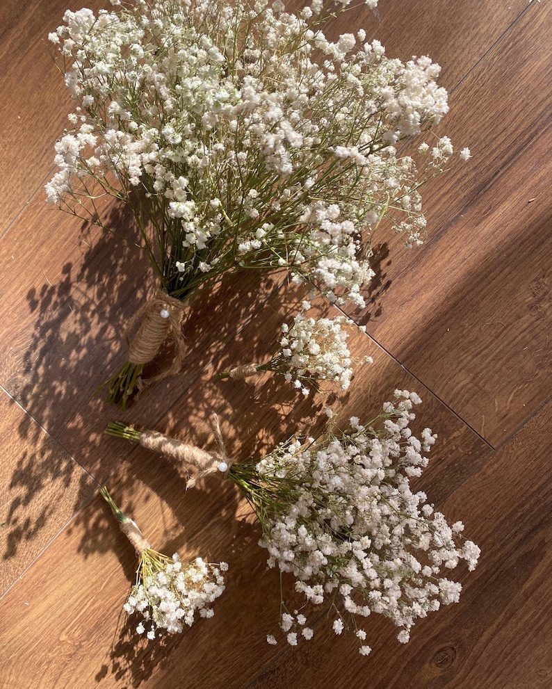 May include: Three bouquets of white baby's breath flowers tied with twine. The bouquets are arranged on a wooden surface.