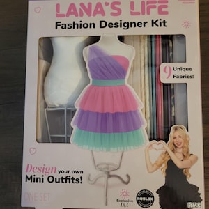 May include: A fashion designer kit with the text "LANA'S LIFE" and "Fashion Designer Kit". The box features a cutout of a dress form wearing a layered, colorful dress. The kit includes 9 unique fabrics and is for ages 8+.