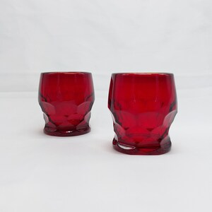 May include: Two red glass shot glasses with a faceted design.