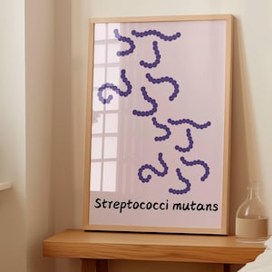 May include: A framed art print featuring a light pink background with abstract blue shapes resembling chains of beads. The text "Streptococci mutans" is printed in black at the bottom of the print. The frame is made of light-colored wood.