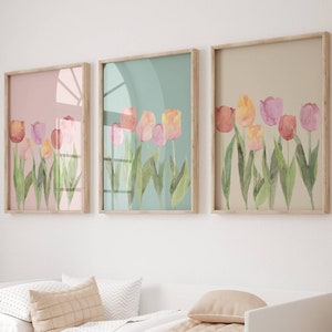 Peut inclure: Trois tableaux encadrés d'aquarelles représentant des tulipes roses, orange et jaunes avec des feuilles vertes sur un mur blanc au-dessus d'un lit d'appoint blanc avec une couverture beige et des oreillers.