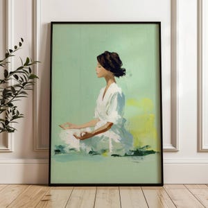 Pode incluir: Impressão de arte emoldurada que retrata uma pessoa em meditação. A figura, vestida de branco, está sobre um fundo verde claro. A obra de arte é emoldurada em preto e exibida em um piso de madeira. Transmite calma.