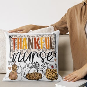 May include: White cushion with a leopard print background and the text "Thankful Nurse" in black and orange. The cushion features a stethoscope, a syringe, and three pumpkins with leopard print accents.