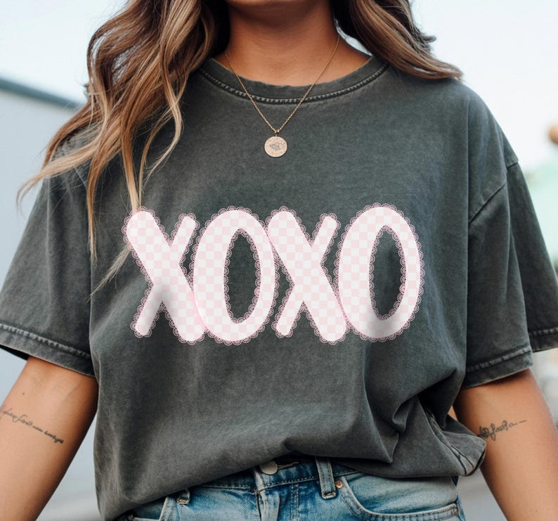 Puede incluir: Camiseta gris oscuro con la palabra "XOXO" en un dise&ntilde;o a cuadros rosa con un borde de encaje blanco. Una prenda informal, adecuada para el uso diario.