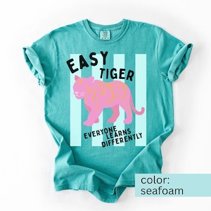 A Comfort Colors 1717 short-sleeved crew neck t-shirt that reads Easy Tiger; Everyone Learns Differently. There is a graphic image of a pink tiger with pale mint green stripes behind the tiger. This shirt is designed for Special Education Teachers working in a school setting.