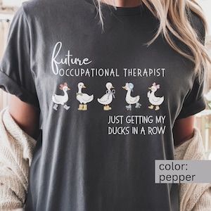 May include: Pepper-colored t-shirt with the text "Future Occupational Therapist" above a row of cartoon ducks. Each duck is accessorized differently. Below the ducks is the phrase "Just Getting My Ducks in a Row."
