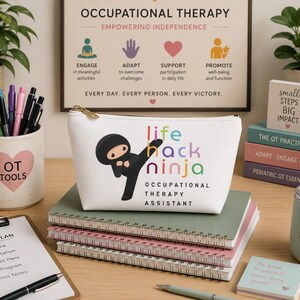 Może przedstawiać: Biały piórnik z zamkiem błyskawicznym, ozdobiony grafiką ninja z kreskówki oraz napisem "life hack ninja OCCUPATIONAL THERAPY ASSISTANT" w kolorowych literach. Piórnik leży na stosie notatników spiralnych na biurku z przyborami biurowymi.