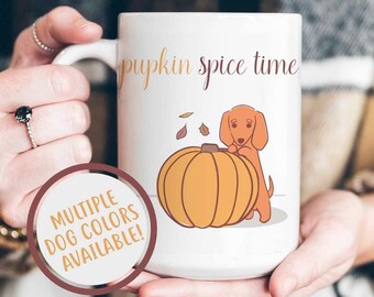 May include: White ceramic mug featuring a brown dachshund dog illustration and the text "pumpkin spice time". The dog is standing next to a large orange pumpkin.
