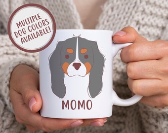 May include: White ceramic mug with a cartoon illustration of a Cavalier King Charles Spaniel dog with brown, black, and white fur. The dog's name "Momo" is printed in brown text below the illustration. The mug has a handle on the right side.