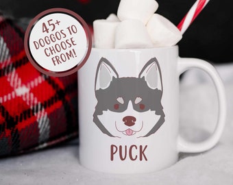 Può includere: Una tazza in ceramica bianca con un'illustrazione di un cane husky di cartone animato e il nome "Puck" stampato sul davanti. La tazza è piena di marshmallow e una cannuccia a righe rosse e bianche.