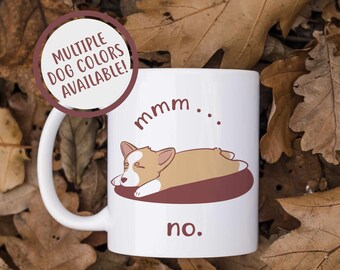Może przedstawiać: Biały kubek ceramiczny z kreskówkowym psem rasy corgi śpiącym na brązowym łóżku. Kubek ma nadrukowany tekst "mmm... nie."