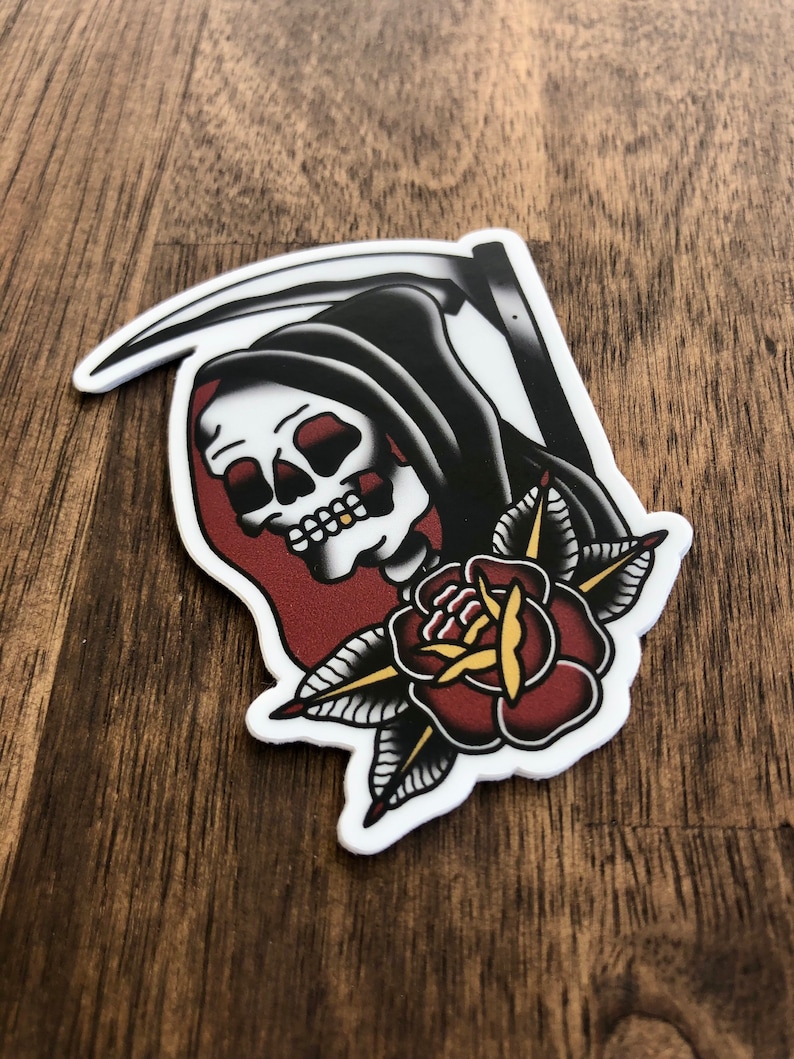 May include: A traditional tattoo style sticker featuring a black hooded figure with a scythe and a red rose with yellow center and green leaves.