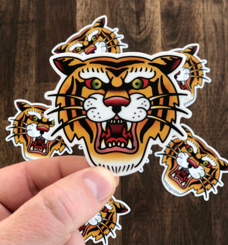 May include: Five colorful tiger head stickers with a traditional tattoo style. The tiger has orange and black stripes, a white face, and red eyes.