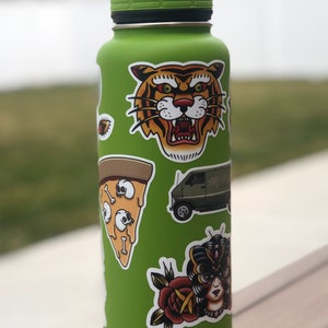 May include: Green reusable water bottle with various stickers, including a tiger face, a pizza slice with skulls, a van with the text "Say Hi", a rose, and a woman with a butterfly mask.