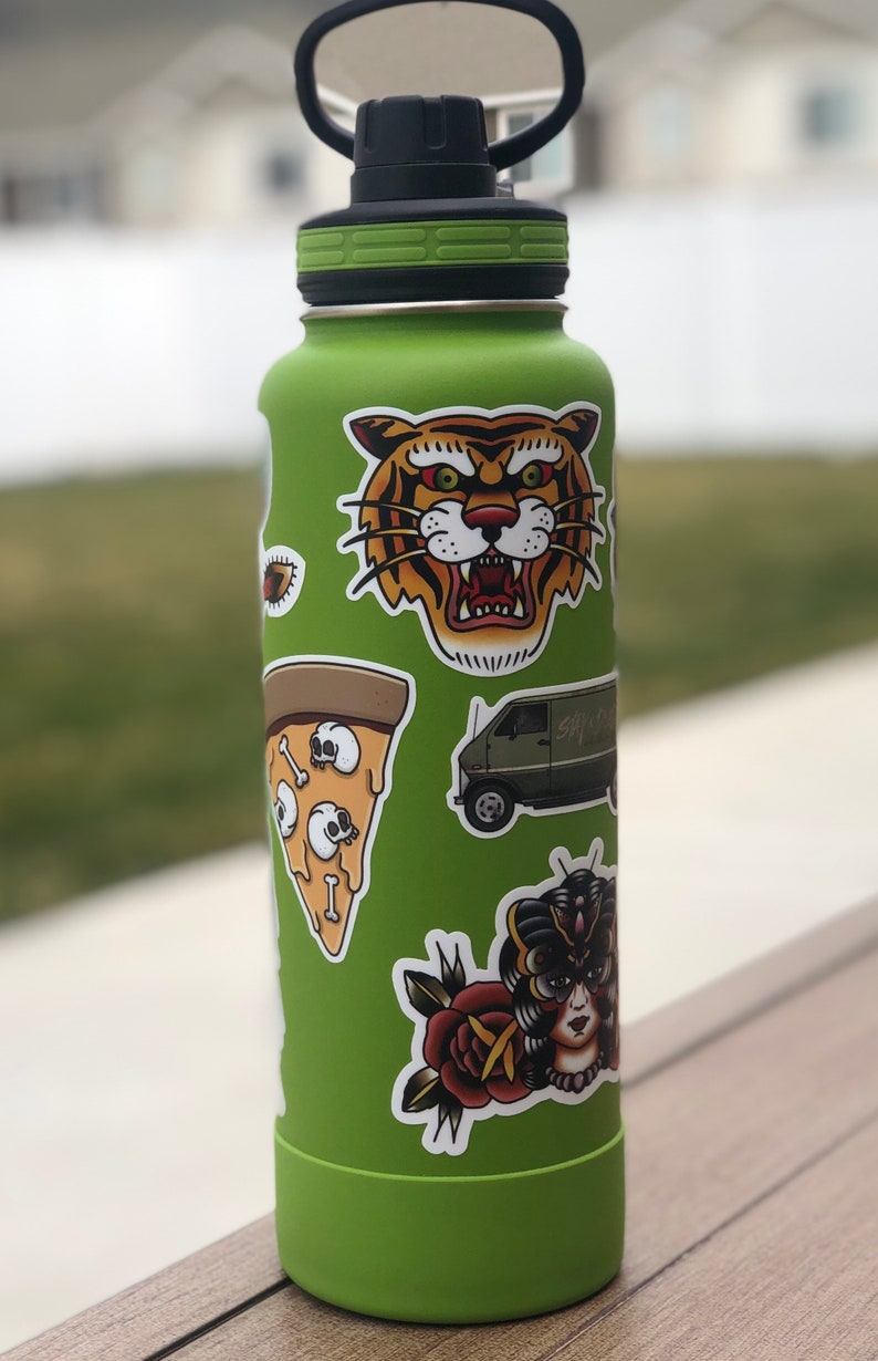 May include: Green reusable water bottle with various stickers, including a tiger face, a pizza slice with skulls, a van with the text "Say Hi", a rose, and a woman with a butterfly mask.