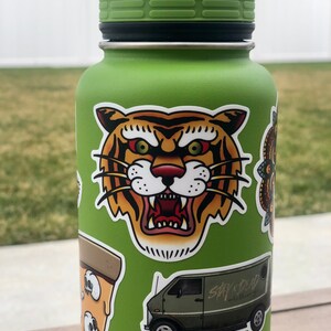 May include: Green reusable water bottle with various stickers, including a tiger face, a pizza slice, a van with the text "Stay Crud" and a butterfly.