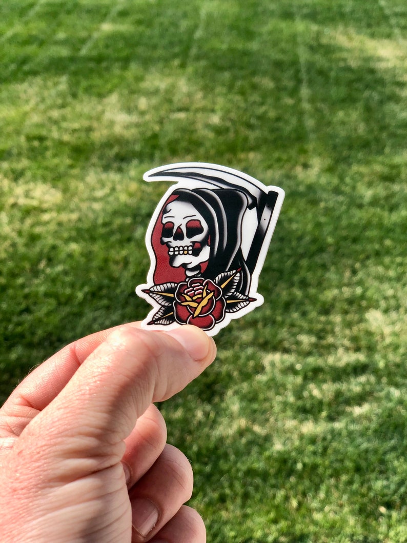 May include: A black and white sticker of the Grim Reaper with a red rose. The Grim Reaper is wearing a black hooded robe and holding a scythe. The rose is red with green leaves.