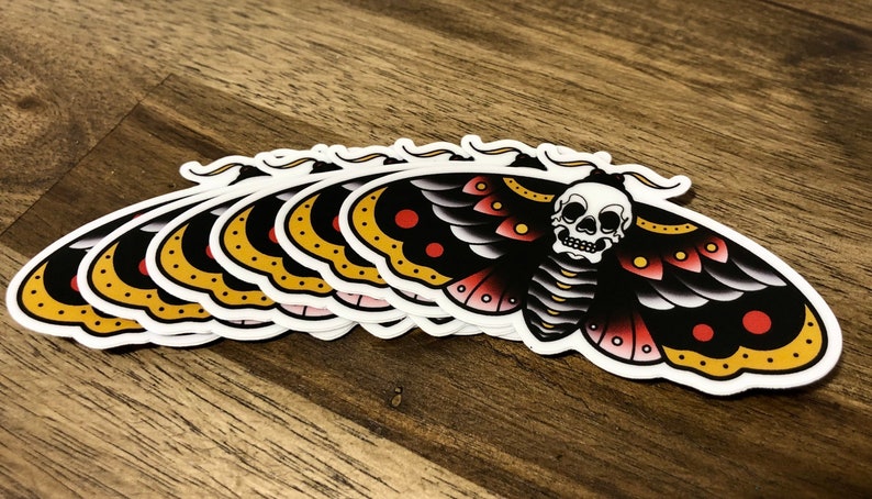 Puede incluir: Un conjunto de ocho pegatinas de polilla negra y amarilla con un dise&ntilde;o de calavera. La polilla tiene detalles rojos y blancos en sus alas.