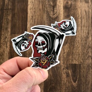 May include: A black and white sticker of the Grim Reaper holding a scythe with a red rose in his hand.