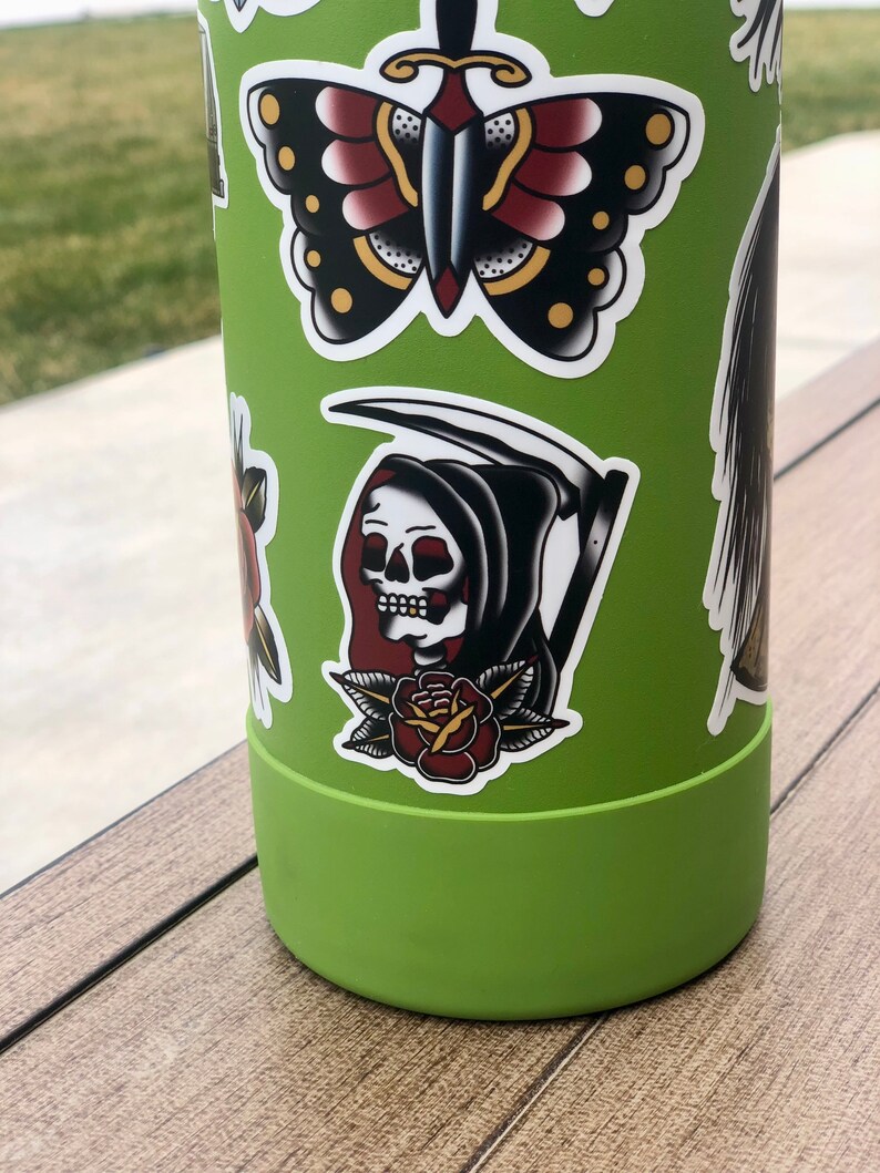 May include: Green reusable water bottle with various colorful stickers, including a butterfly, a grim reaper with a scythe, and a rose.