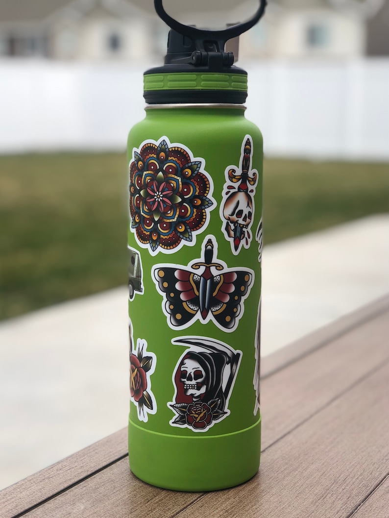 May include: A green reusable water bottle with various colorful stickers, including a mandala, a butterfly, a skull with a dagger, and a grim reaper.