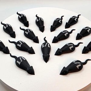 May include: A collection of black mouse figurines with white accents, arranged on a white circular surface. Each mouse has a long, curved tail and a white design on its back. The figurines are evenly spaced, creating a visually appealing pattern.