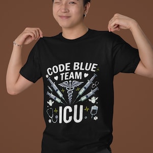 May include: A black t-shirt featuring a graphic print with the text CODE BLUE TEAM ICU. The design includes a central caduceus symbol, four syringes, two anatomical hearts, a stethoscope, and an IV bag, all rendered in white, blue, and yellow.