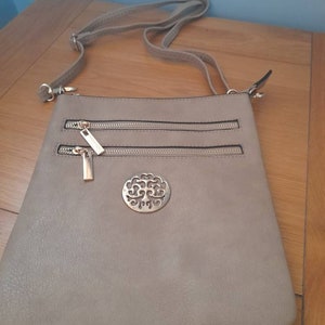 May include: A beige crossbody bag with a gold zipper and a decorative gold circle with a tree design.