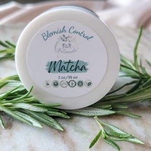 May include: A white jar with a green and white label that reads "Blemish Control R&P Botanicals Matcha 2 oz/59 ml". The jar is surrounded by sprigs of rosemary.