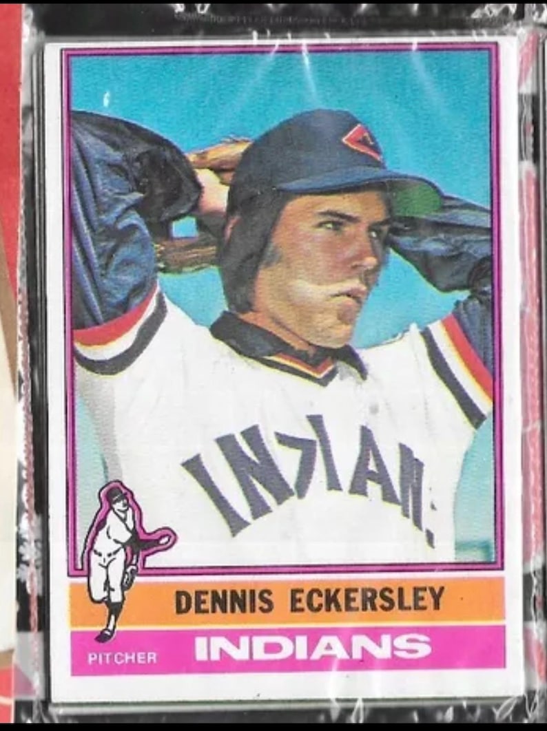 Puede incluir: Una tarjeta de b&eacute;isbol con Dennis Eckersley, un lanzador de los Indios de Cleveland. La tarjeta es del set de tarjetas de b&eacute;isbol Topps de 1977. La tarjeta presenta una foto a color de Eckersley con su uniforme de los Indios, con el logotipo del equipo en su gorra. La tarjeta tambi&eacute;n incluye el nombre, la posici&oacute;n y el nombre del equipo de Eckersley.