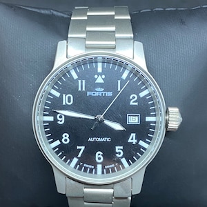 May include: A stainless steel Fortis automatic watch with a black face. The watch has white numerals, hands, and a date display at 3 o'clock. The watch strap is also stainless steel.
